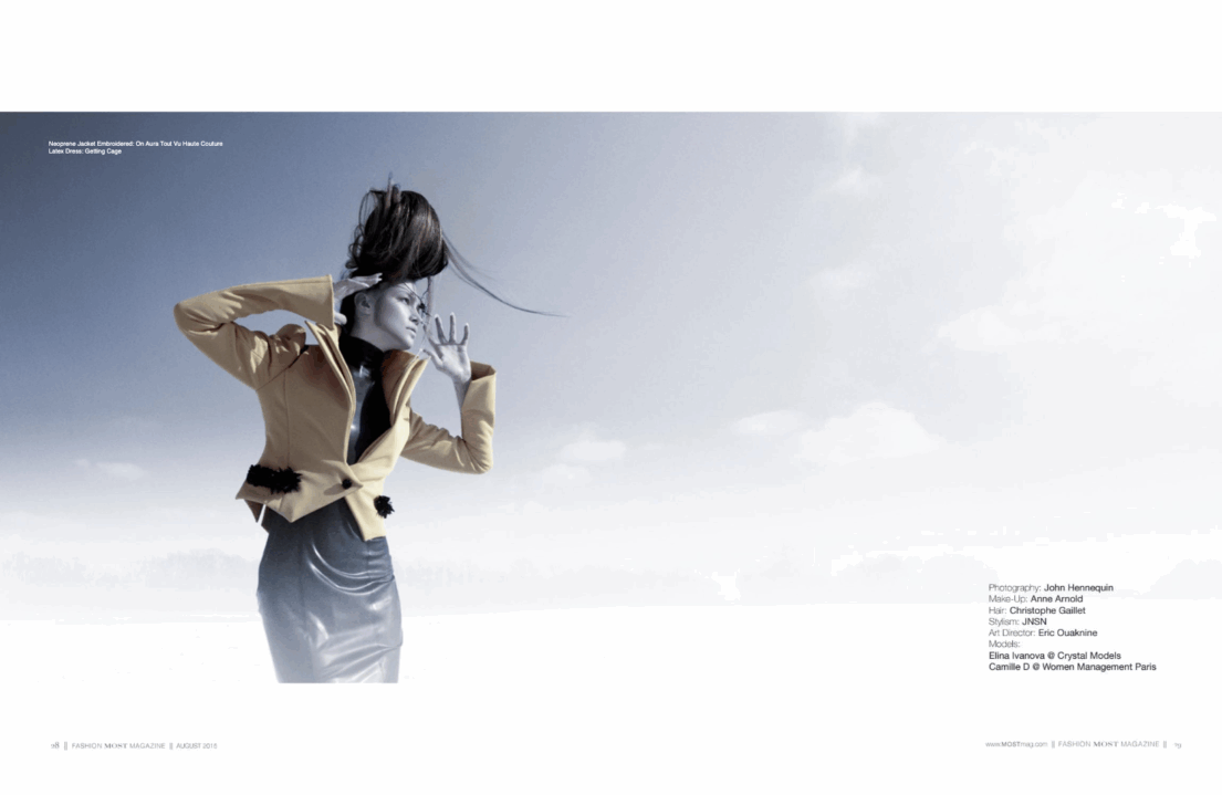 Woman in beige jacket with hair blowing in wind against blue sky.