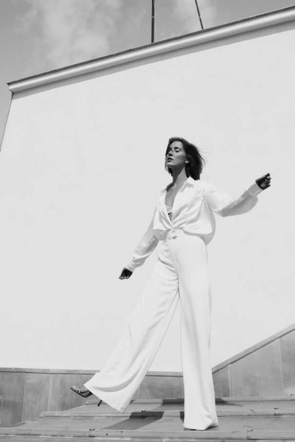 Woman in white attire striking a dynamic pose against a roof minimalist backdrop.