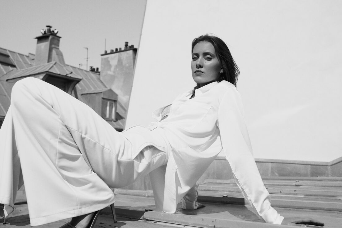 Woman in white attire lounging on rooftop with Paris backdrop.
