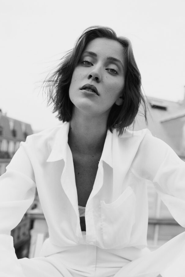 Woman in white shirt with short hair, seated outdoors against urban backdrop.