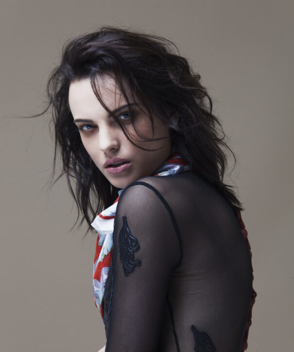 Woman with dark hair wearing sheer black top and patterned scarf.