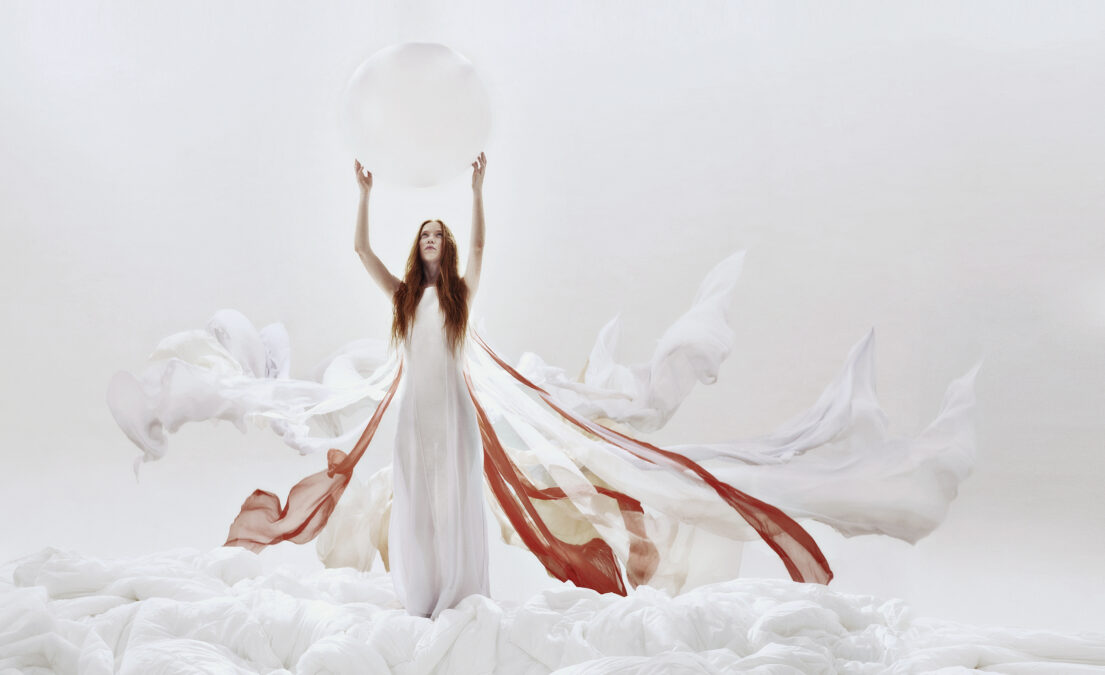 Woman in white dress with flowing red accents, holding a translucent Moon amidst abstract forms.