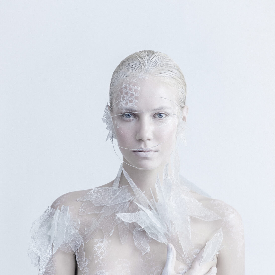 Woman with white hair and lace-like material over her face and shoulders.