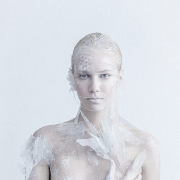 Woman with white hair and lace-like material over her face and shoulders.