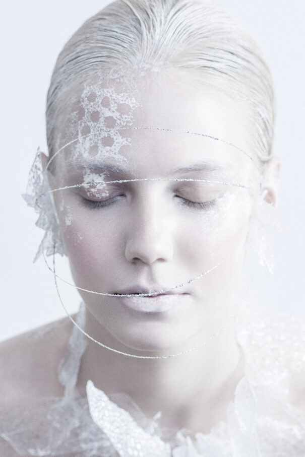 Close-up of a woman with silver hair and eyes closed, adorned with white lace and metallic thread.