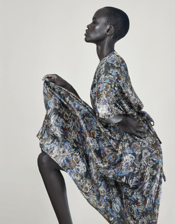 A woman model in an ornate floral dress with short hair, set against a neutral background.