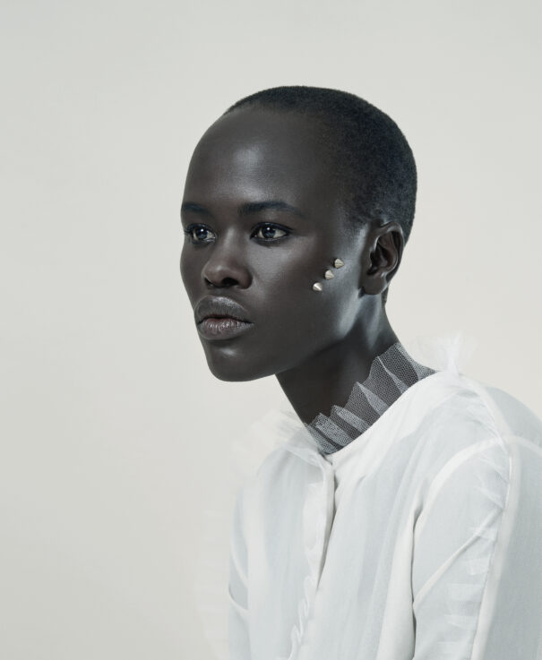Black woman with short hair, wearing white attire and silver facial gems.