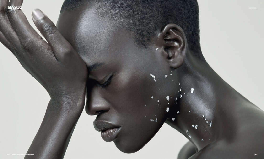 A contemplative individual with short hair, closed eyes, and white speckles on their skin, hand resting on forehead.