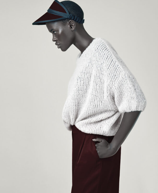 A woman wearing a white knit sweater and burgundy pants with hands on hips.