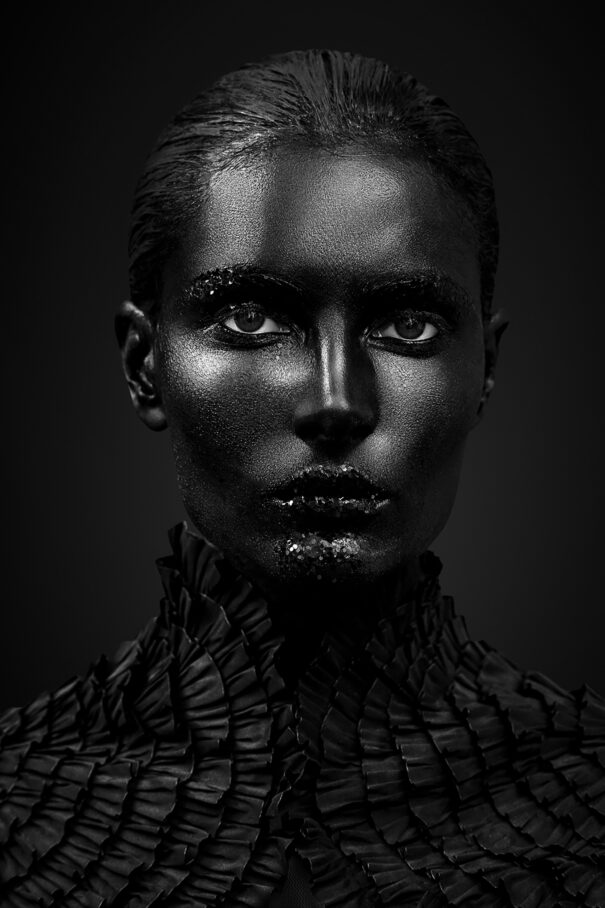Black and white portrait of an individual with dramatic makeup and textured attire.