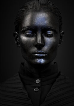 A person with metallic blue makeup against a black background.
