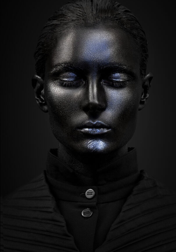 A person with metallic blue makeup against a black background.