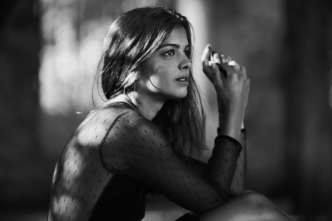 Anais Parello in black sheer top with natural lighting and shadow play.