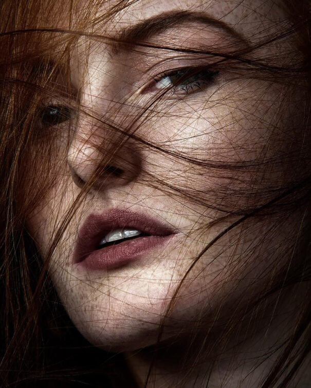 Red-haired woman with hair obscuring her face, intense gaze."