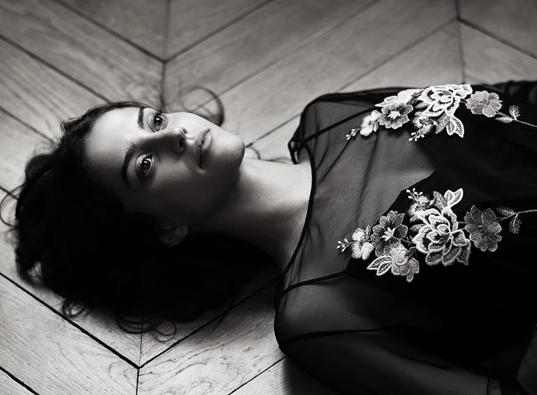 Woman lying on wooden floor in black lace top with floral embroidery.