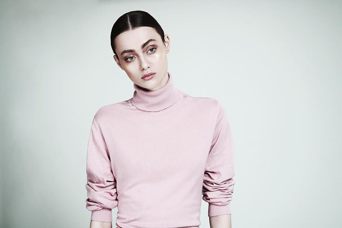 Woman in pink turtleneck with sleek hairstyle against plain background.