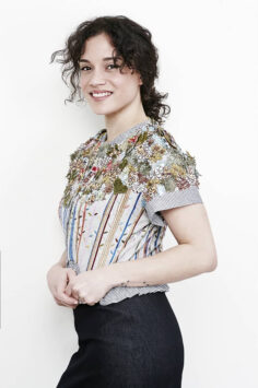 Honorine Magnier, Curly-haired woman in floral-patterned top with striped accents and black pants.
