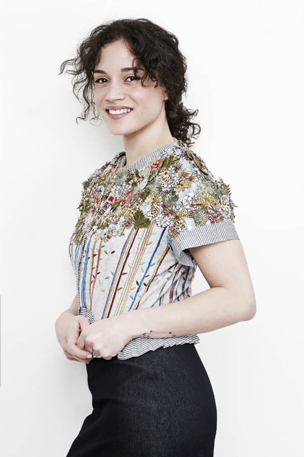 Honorine Magnier, Curly-haired woman in floral-patterned top with striped accents and black pants.