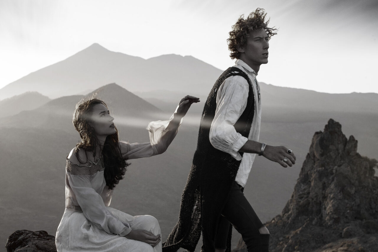 A man and woman in vintage attire explore rugged terrain at sunset.
