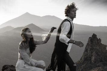 A man and woman in vintage attire explore rugged terrain at sunset.