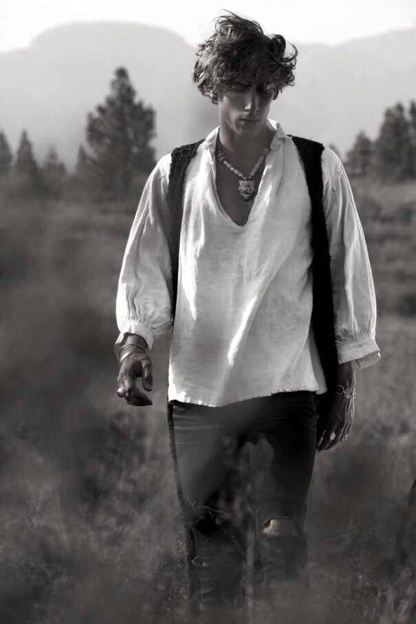 Man in historical attire walking through a field with mountains in the background.