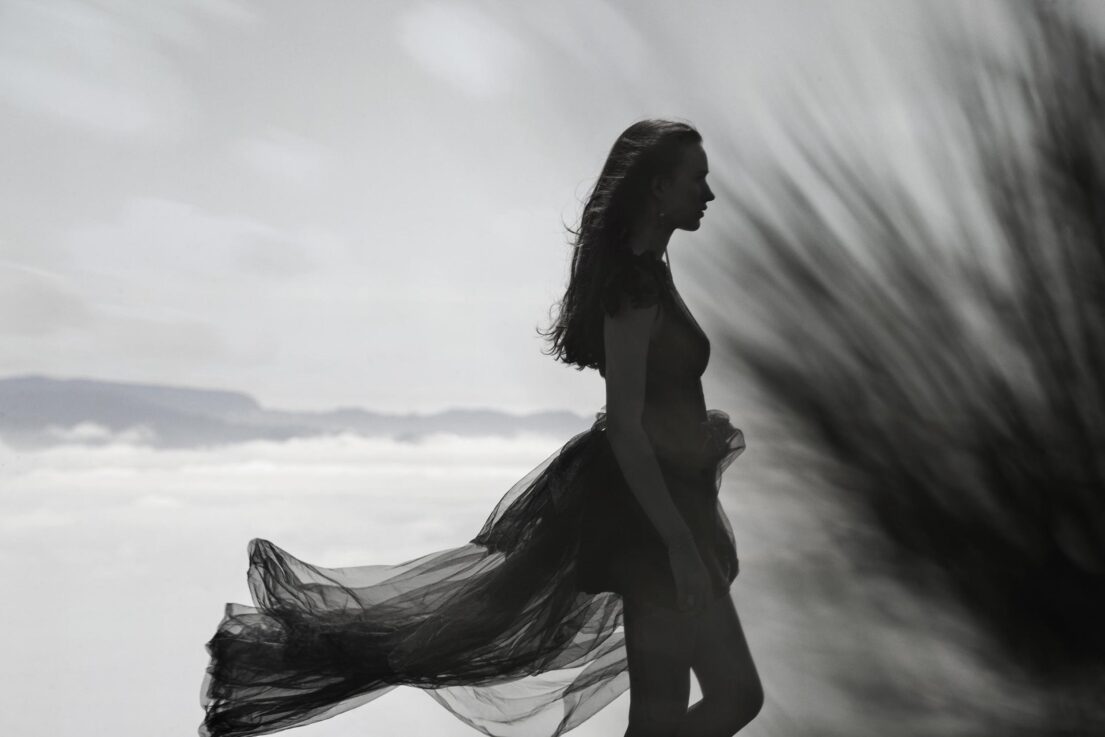 Silhouette of a woman with flowing dress against a cloudy sky.