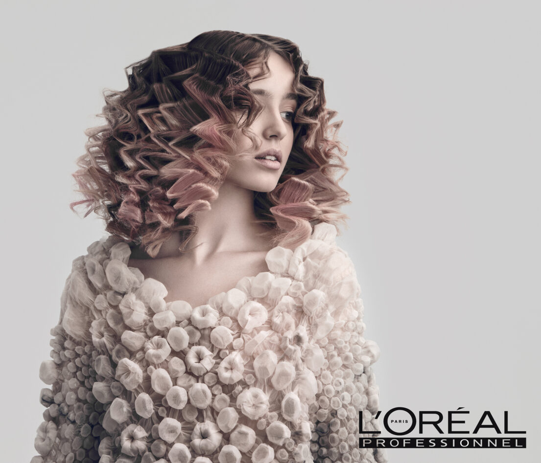 Curly hair with pink tones, textured fabric garment, L'Oréal Professionnel branding.